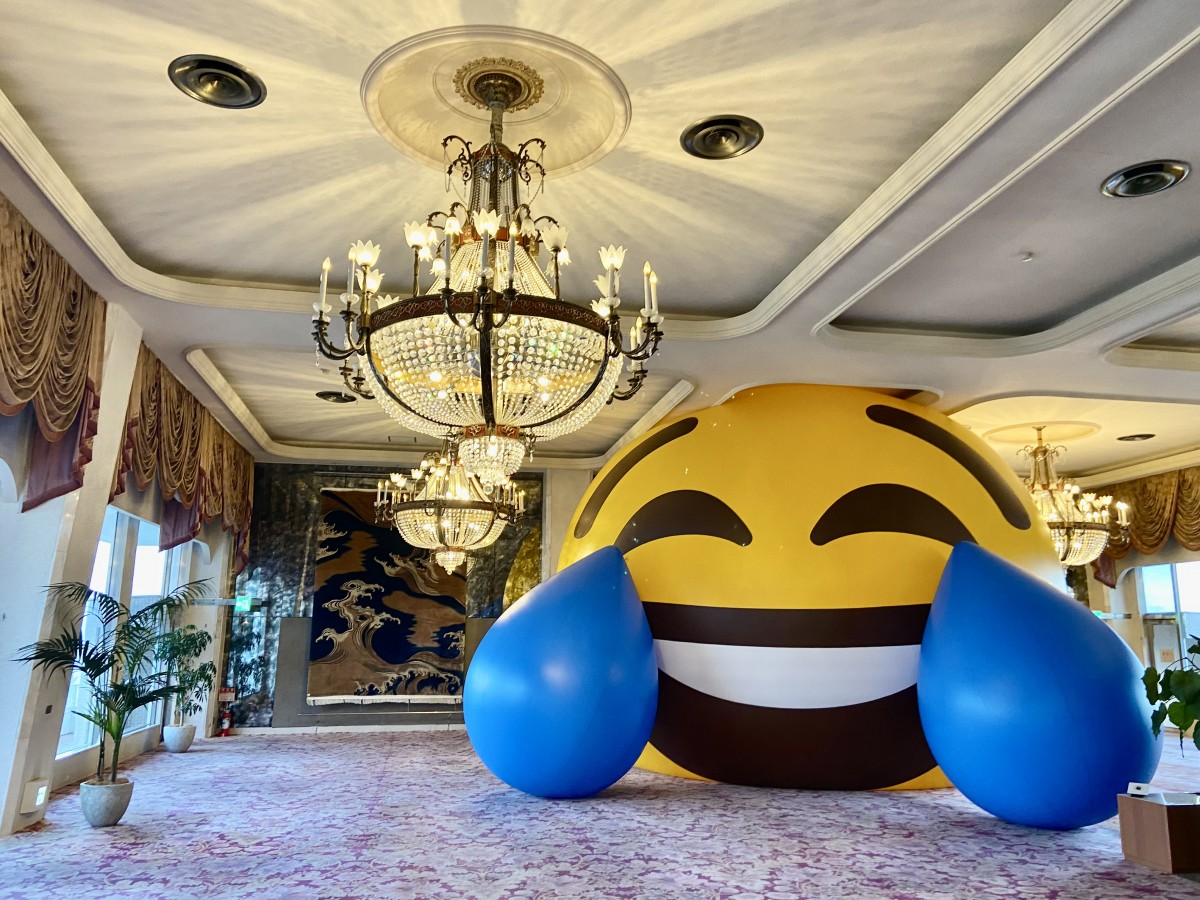 数年前、熱海の老舗ホテル『ニューアカオ』にて展示されていたアート（松田将英『The Big Flat Now』）。小津安二郎の『東京物語』でも描かれたこの熱海の地に、突如現れた巨大な「笑い泣き」の絵文字。デジタル上の感情が現実空間を占領するその姿は、私たちが直面している「ゼロ距離」社会の縮図のようでもあります。