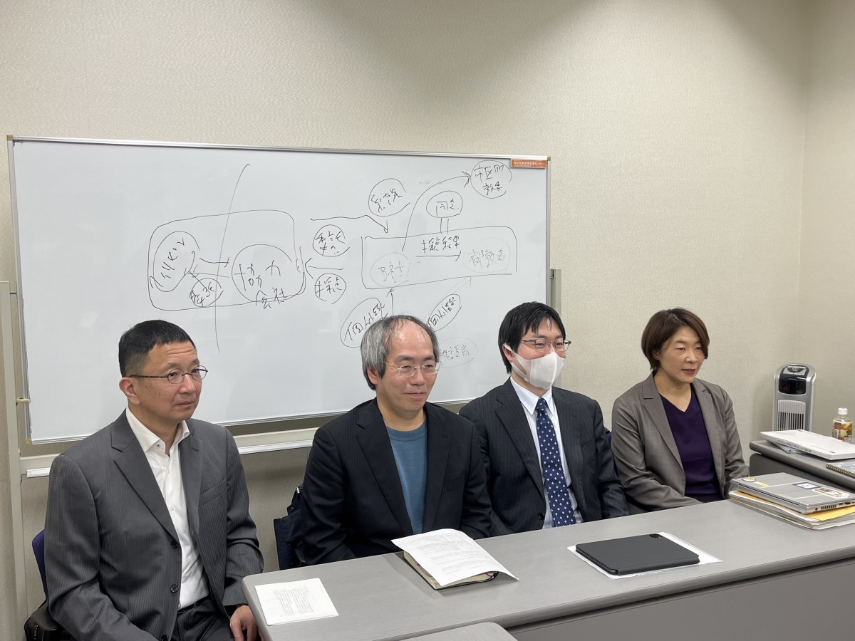 左から原告の吉田弘幸氏、大内裕和氏、大島義則弁護士、出口かおり弁護士(2023年12月6日 第1回 口頭弁論終了後、場所を移して実施された傍聴者への報告会) *後方のホワイトボードは非常に複雑な個人情報の論点説明に使用