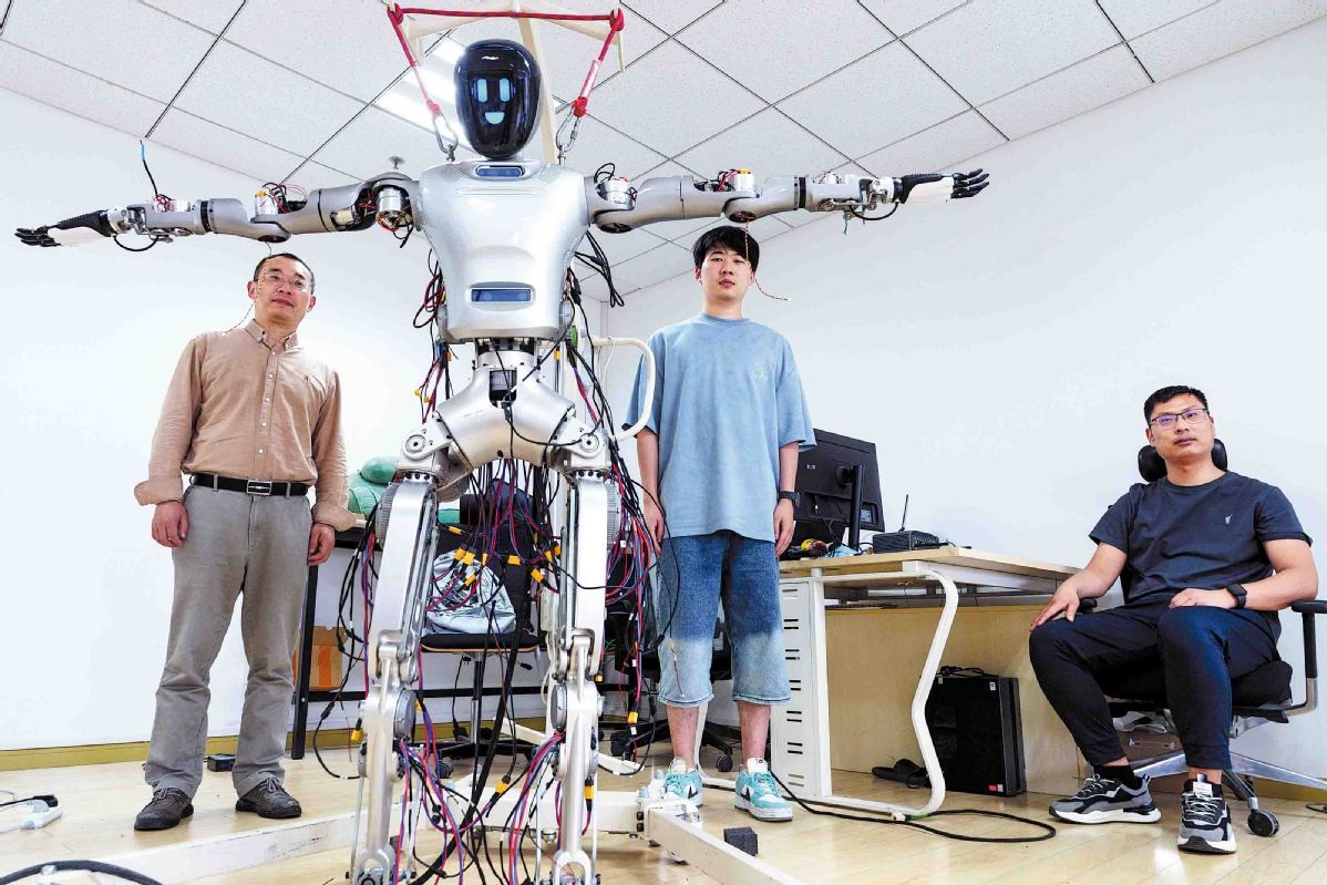 上海の復旦大学でヒューマノイドロボット・プロジェクトを率いる劉立正氏（左）とチームのメンバーが、高齢者向けヘルスケア用途に開発したヒューマノイドロボット「光華1号」と共に写真に収まった。[写真：GAO ERQIANG/CHINA DAILY]