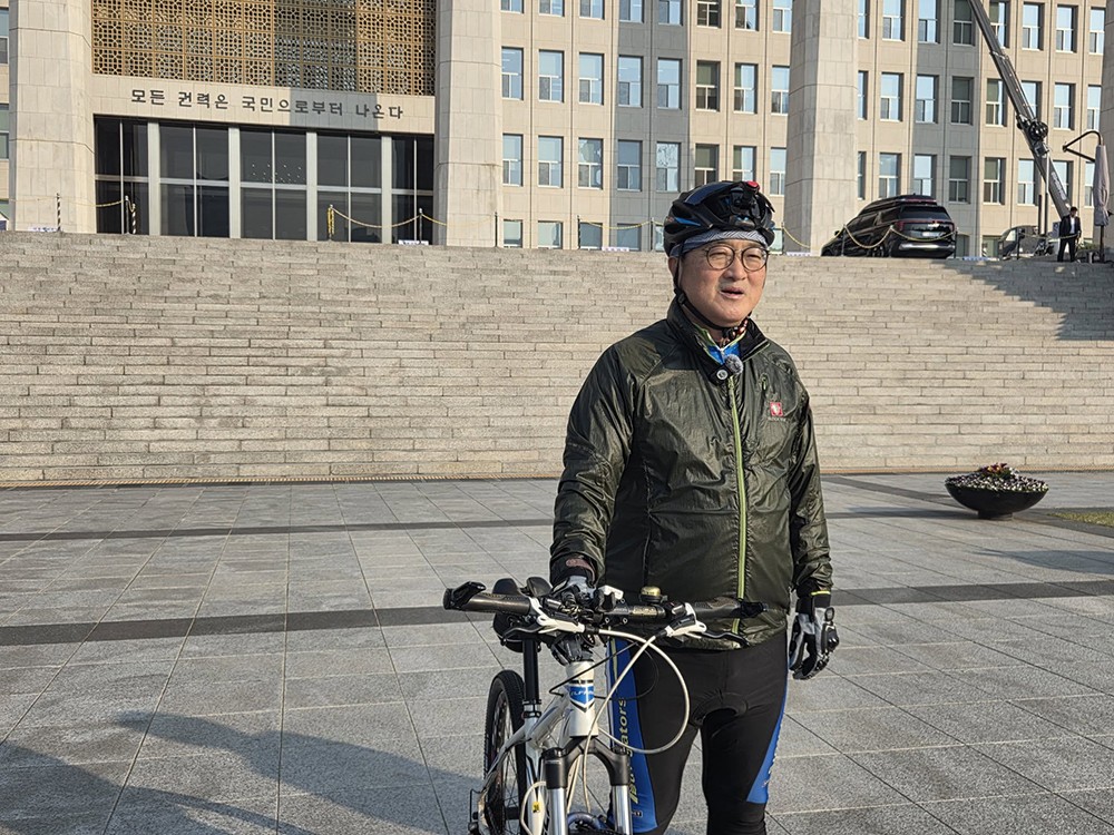 2日、エネルギー節約のため自転車で国会へと出勤した禹元植議長。背景の国会本会議上には「すべての権力は国民から生じる」という文句が刻まれている。これは憲法1条2項「大韓民国の主権は国民にあり、すべての権力は国民から生じる」から取られたもので、非常戒厳阻止(早期解除)から一年にあたる昨年12月3日に合わせ新たに刻まれた。Facebookより引用。