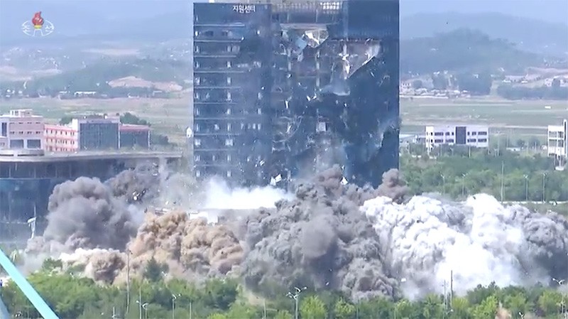 20年6月、朝鮮が南北共同連絡事務所を爆破した際の映像をキャプチャしたもの。煙の中に連絡事務所がある。後方の大きな建物が開城工団総合支援センター。朝鮮中央通信より。