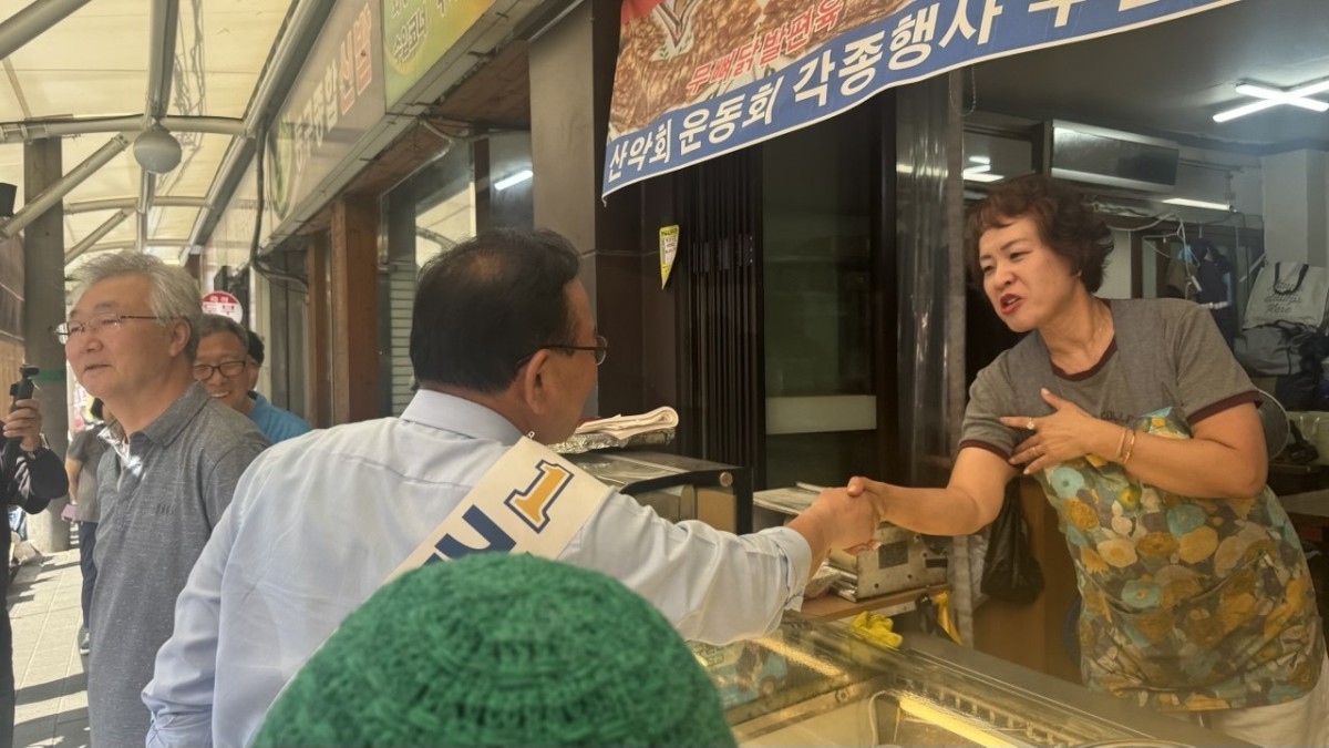 市場の店を一軒一軒たずね、握手する金富謙氏(たすきの人物)。筆者撮影。