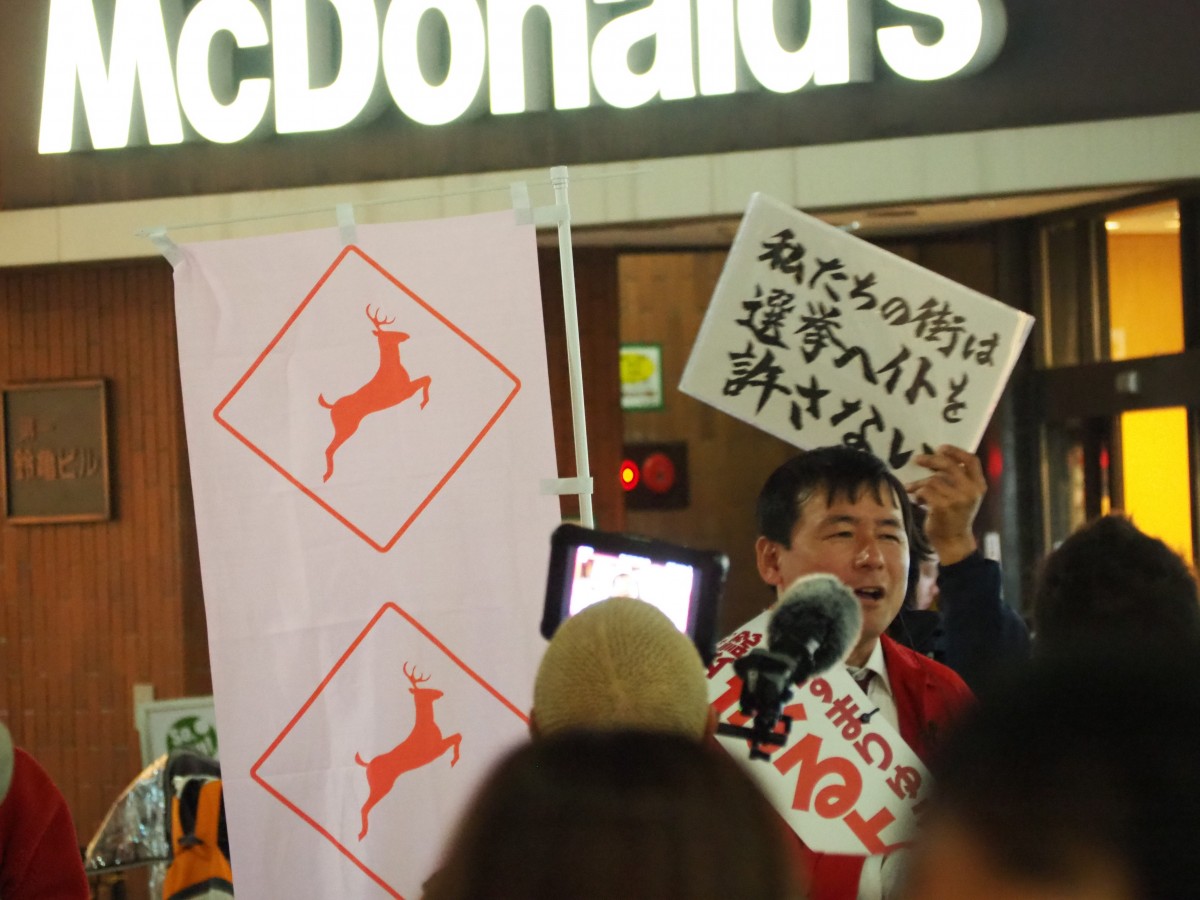 （まるよし候補と抗議のプラカード）