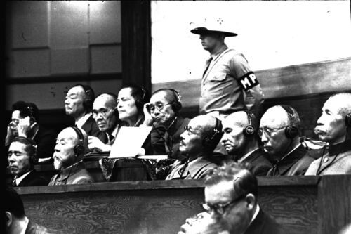 1946年6月、東京・市ケ谷の極東国際軍事裁判所で開かれた東京裁判（極東国際軍事裁判）の被告席。イヤホンをつけキーナン首席検事の論告に聞き入る（右から）荒木貞夫、梅津美治郎、岡敬純、東条英機、松井石根、大島浩、永野修身、小磯国昭、南次郎、橋本欣五郎（左手を上げている）、広田弘毅の各被告