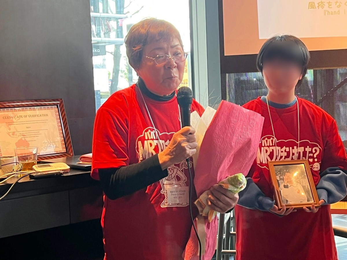 娘の妙子さんの写真のそばで挨拶する可児佳代さん