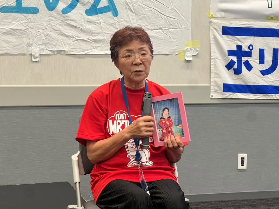 妙子さんの写真を手に持って体験を語る可児佳代さん