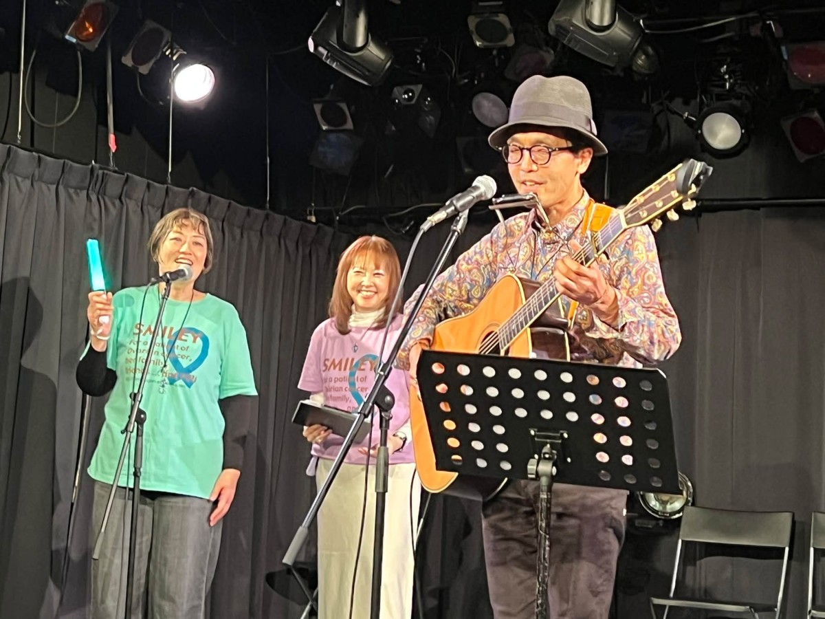 設立当初から協力してきた腫瘍内科医、勝俣範之さん（右）の歌に合わせてコーラスを歌うスマイリー代表の片木美穂さん（左）とさくらさん（真ん中）