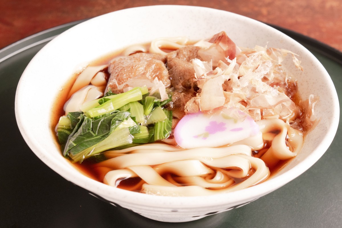 きしめん680円。濃い茶褐色のつゆに白く幅のある麺が映える。かまぼこの絵柄は季節により変わる。ほうれん草ではなく小松菜がトッピングされているのも珍しい
