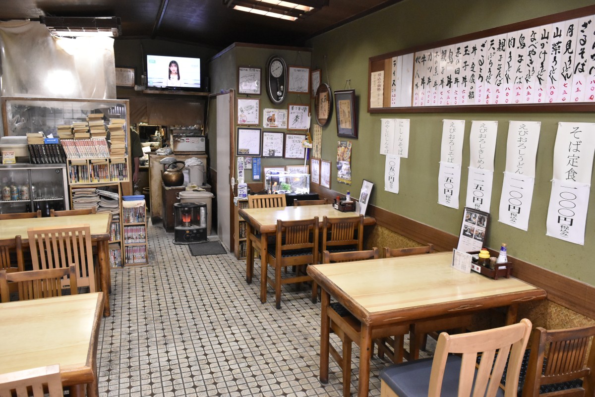 いかにも昔ながらの麺類食堂といった趣の店内。6卓で24席。筆文字の品書きも老舗然とした味がある
