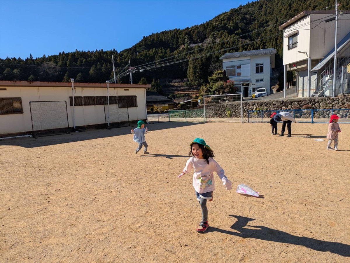 年あけ、凧揚げを楽しむ娘。向かって左の横長のプレハブが保育所。走っているのは小中学校の校庭で、娘は校庭を「公園」と呼ぶ