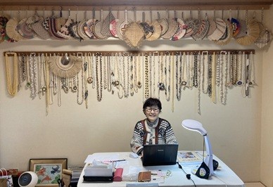 オフィスの一盛さん。後ろは、南太平洋の島国で貰った団扇とレイ。手作りの貝殻レイをお客さんにかける習慣があると聞き、「お花ではなく貝殻！」と驚いた。貝殻が島ごとに違うのも興味深い。